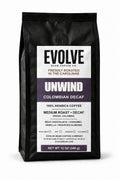 12 oz black bag of Evolve Bean UNWIND Colombian Decaf coffee with a white and purple label on a white background.